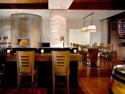 Moderní hotelový bar s dřevěnými židlemi, krbem a elegantní jídelnou za teplého osvětlení.