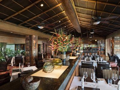 Elegantní hotelová restaurace s dřevěným nábytkem, velkými okny a centrální květinovou dekorací.