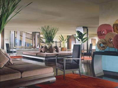 Modern eingerichteter Wohnzimmerbereich mit Sofas, Sesseln, Teppichen und großen Pflanzen.