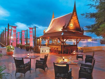 Gemütliche Sitzgelegenheiten und eine traditionelle thailändische Hütte bei Sonnenuntergang am Wasser.