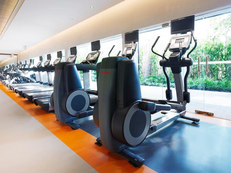 Moderner Fitnessraum mit Rudergeräten und Crosstrainern vor großen Fenstern mit Blick ins Grüne.