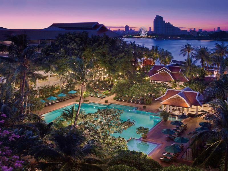 Abendliche Ansicht eines Resorts mit beleuchtetem Pool und Palmen am Wasser.