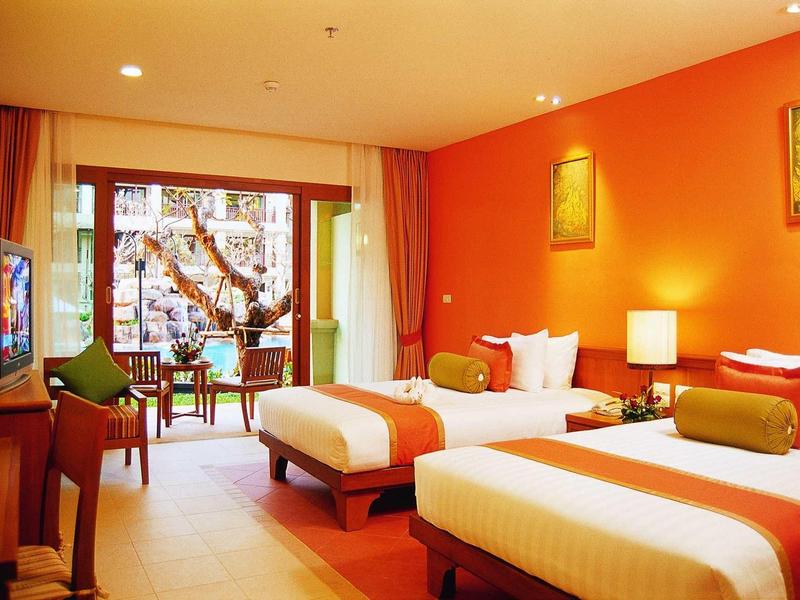 Helles Hotelzimmer mit zwei Betten, orangenen Wänden, Fensterfront und Balkon mit Tisch und Stühlen.