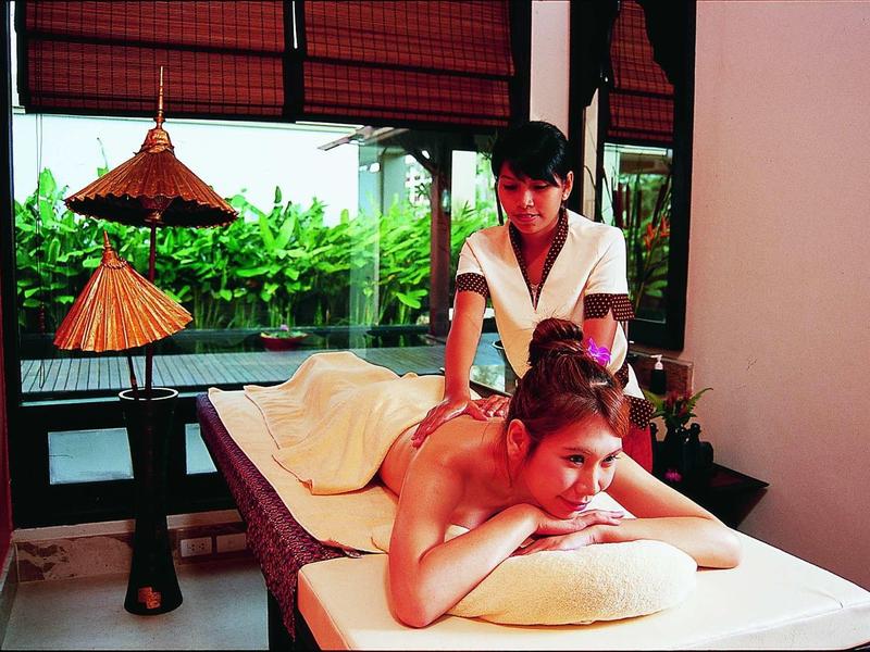 Frau erhält Rückenmassage auf Liege in heller, moderner Wellness-Oase mit großen Fenstern.