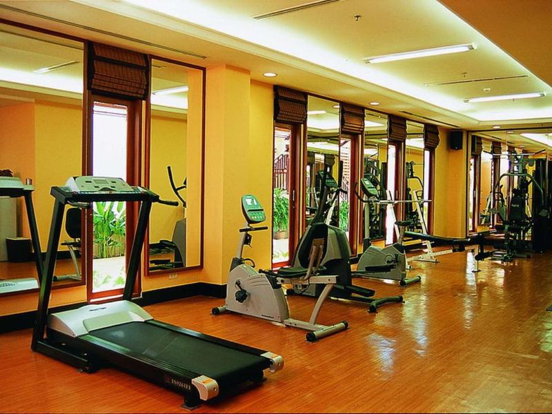 Gut beleuchteter Fitnessraum mit Laufband, Heimtrainer und Kraftgeräten vor großen Spiegeln.