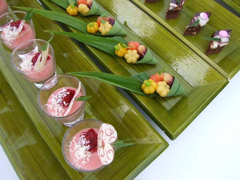 Mehrere Gläser mit rosa Creme und kleinen bunten Süßigkeiten auf grüner Platte angeordnet.