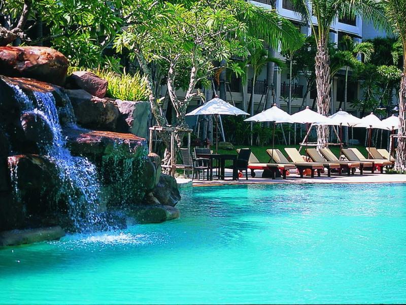 Klares türkisfarbenes Poolwasser mit Wasserfall, Liegestühlen und Sonnenschirmen in tropischer Umgebung.