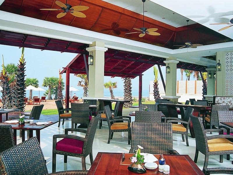 Offener Restaurantbereich mit Holztischen, geflochtenen Stühlen und buntem Deckendekor.