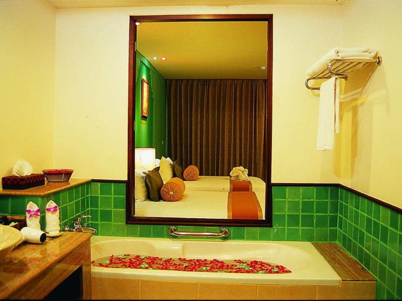 Badezimmer mit grün gekachelter Badewanne, großem Spiegel und Blick ins Schlafzimmer mit Bett.