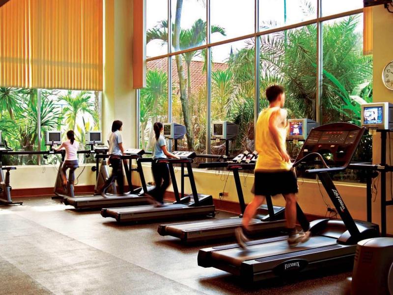 Fitnessraum mit großen Fenstern, mehreren Laufbändern und einer Person beim Joggen.