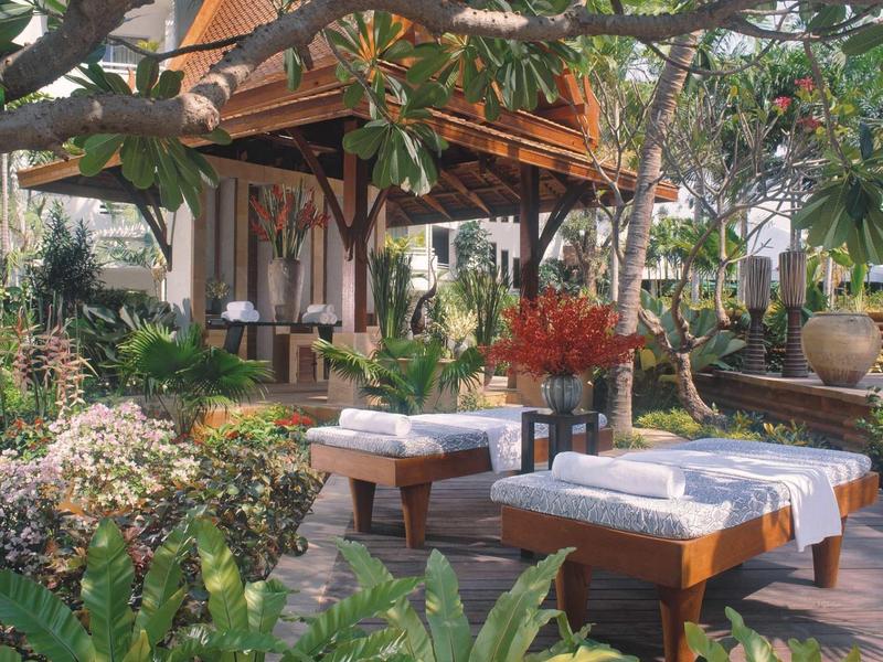 Garten mit zwei Massageliegen, üppigem Grün und Holzhütte im Hintergrund bei Tageslicht.