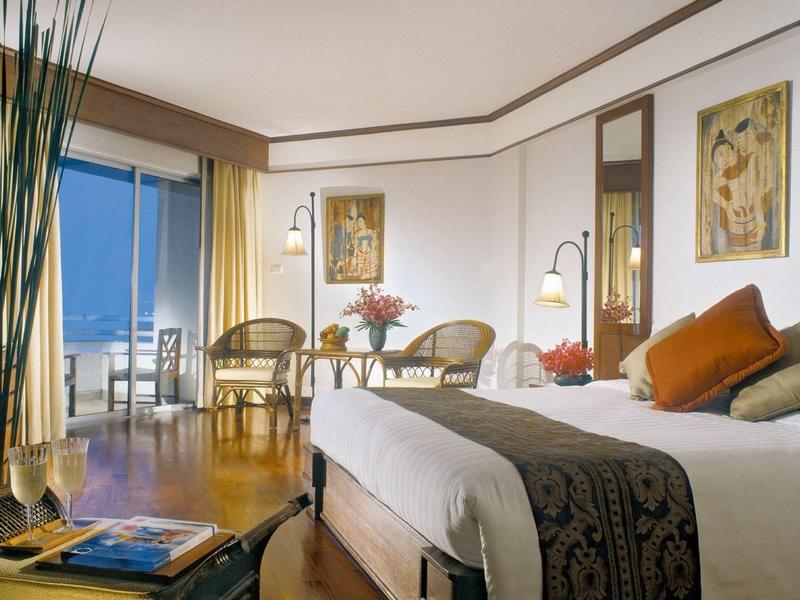 Helles Schlafzimmer mit Doppelbett, Holzfußboden, zwei Stühlen, Tisch und Blick auf den Balkon.