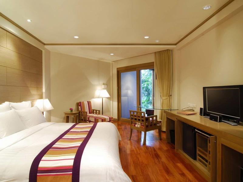 Helles Hotelzimmer mit großem Bett, Holzboden, Fernseher, Schreibtisch und Zugang zu Gartenbereich.