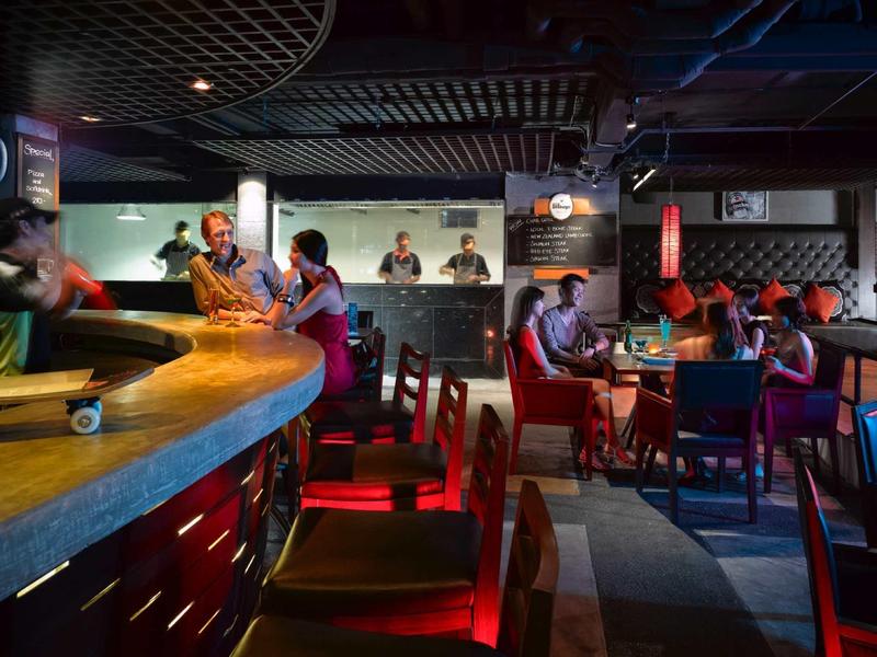 Gemütliche Bar mit Holztheke, roten Sitzgelegenheiten und gedämpfter, bunter Beleuchtung.