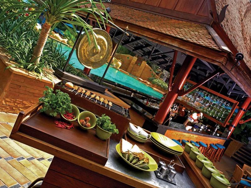 Outdoor-Küche mit Holztheke, frischen Kräutern, Tellern und tropischem Pool im Hintergrund.