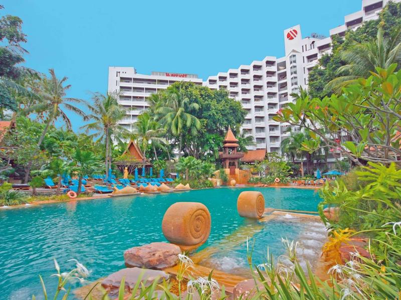 Großer Pool mit Wasserfällen und Planschbecken, umgeben von Palmen und Hotelgebäude im Hintergrund.