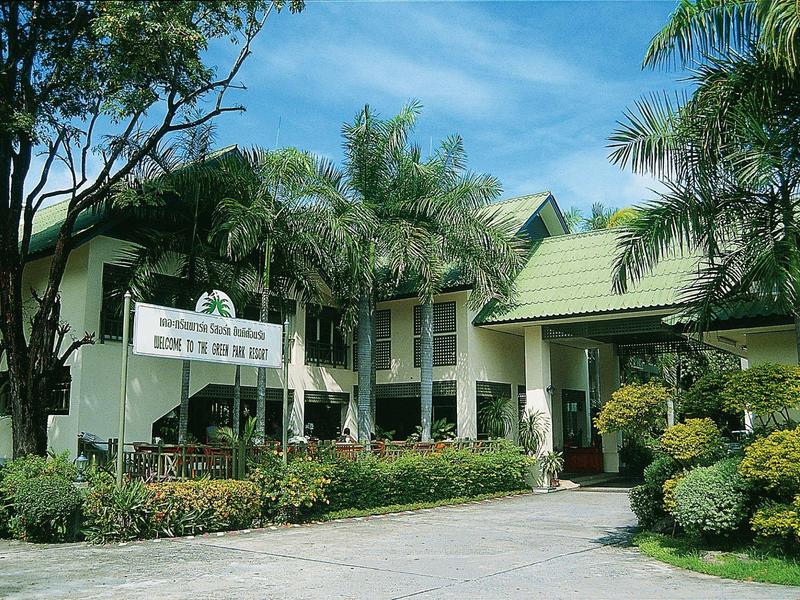 Gebäude mit grünem Dach, umgeben von Palmen und üppigem Grün unter blauem Himmel.