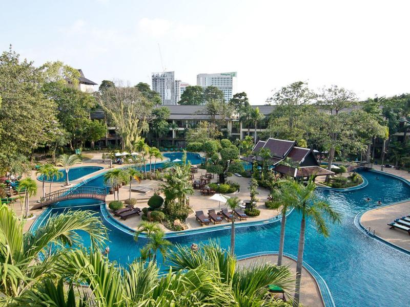 Großer Hotelpool mit geschwungenen Becken, Palmen, Liegen und grüner Gartenanlage bei klarem Himmel.