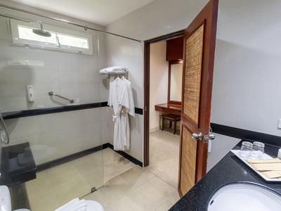 Helles Badezimmer mit weißem Waschtisch, Handtüchern, Bademänteln und offenem Holztürrahmen.