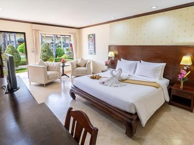 Helles Schlafzimmer mit großem Bett, Sesseln am Fenster und Fernseher auf Holzständer.