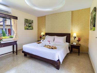 Helles Schlafzimmer mit Doppelbett, Holzmöbeln, Wandbildern und offener Fensterfront.