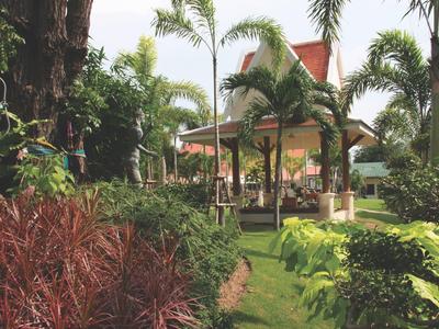 Garten mit üppigem Grün, Palmen und Pavillon mit rotem Dach im Hintergrund.