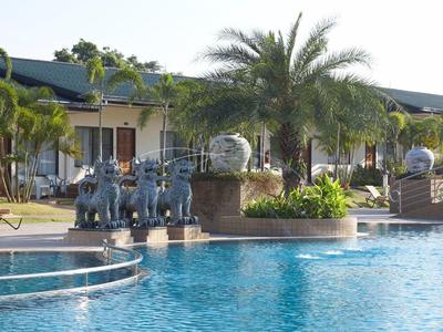 Ein Pool vor Gebäuden, umgeben von Palmen und Elefanten-Skulpturen, bei Sonnenschein.