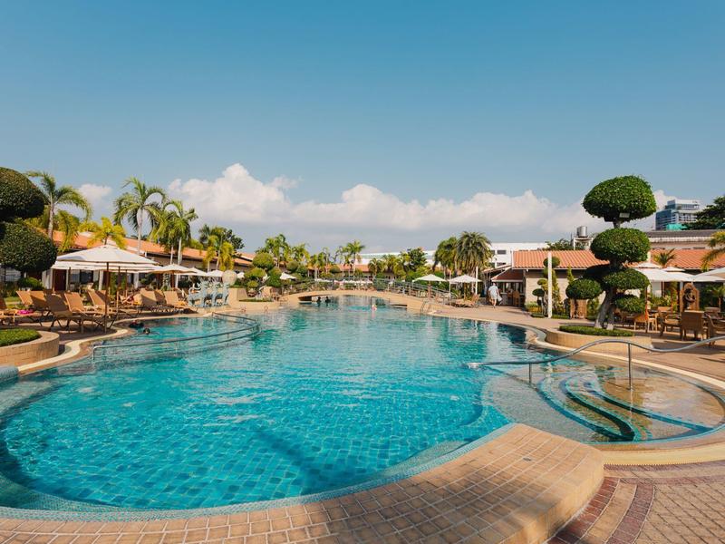 Großer Pool mit klarem Wasser umgeben von Sonnenschirmen, Liegestühlen und gepflegten Bäumen.