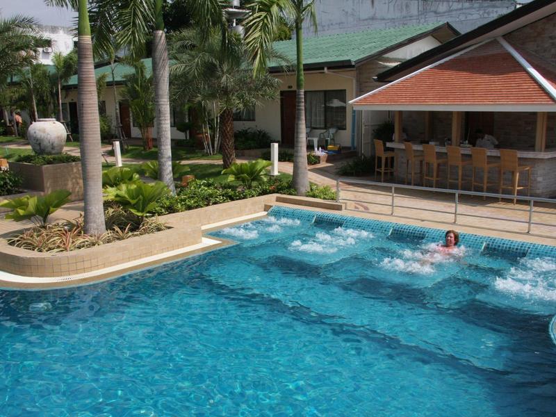 Schwimmbad mit rein blauem Wasser, Palmen und einer Poolbar im Hintergrund bei sonnigem Wetter.