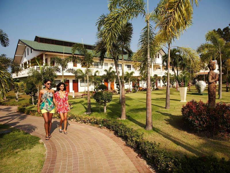 Zwei Frauen gehen auf einem gepflasterten Weg vorbei an Palmen und großen weißen Gebäuden.