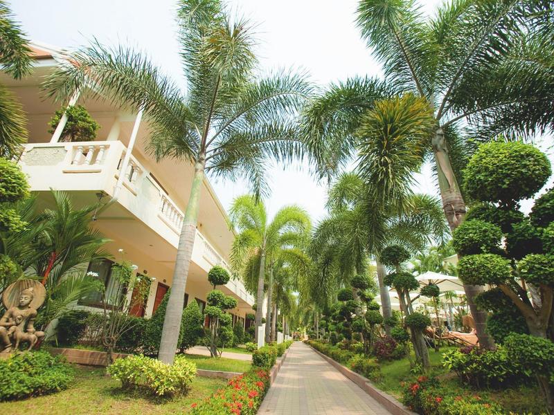 Ein Gartenweg mit Palmen und gepflegten Büschen neben einem hellen Haus.