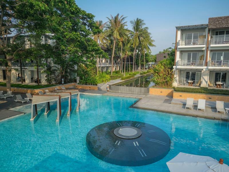 Ein moderner Pool mit runden Wasserspielelementen, Sonnenschirmen und Palmen im Hintergrund.