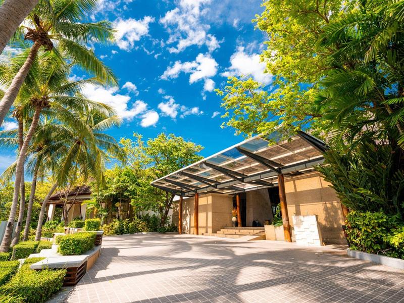 Moderne Villa mit großer Terrasse, umgeben von Palmen und üppigem Grün bei blauem Himmel.