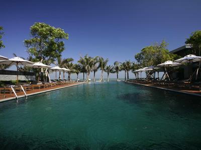 Großer Pool mit Liegestühlen und Sonnenschirmen neben Palmen unter klarem blauem Himmel.