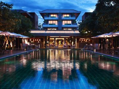 Illuminated pool in front of a multi-story hotel building at dusk.