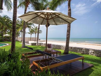 Liegestühle mit Sonnenschirm unter Palmen am Strand bei klarem Himmel.