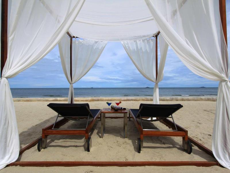 Two lounge chairs under a white canopy facing the beach and sea.