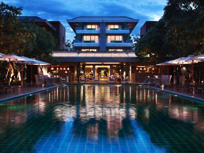 Illuminated pool in front of a multi-story hotel building at dusk.