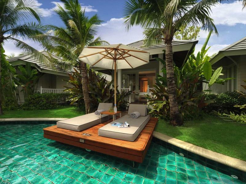 Two lounge chairs with umbrella on wooden platform in pool at tropical hotel.