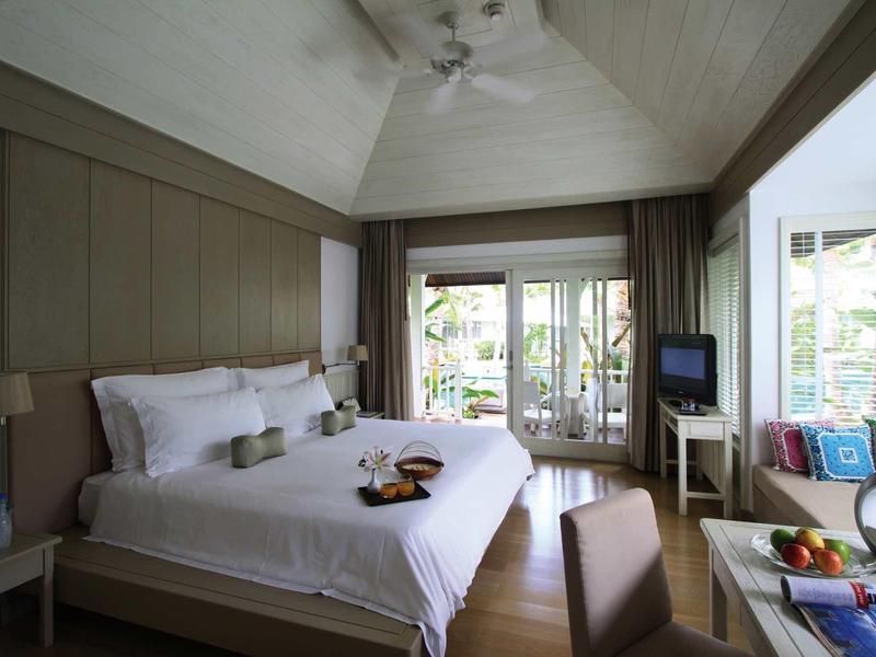 Bright hotel room with large bed, TV, window wall, and seating area overlooking greenery.