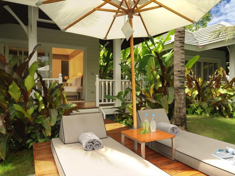 Two lounge chairs with umbrella next to tropical garden and veranda.