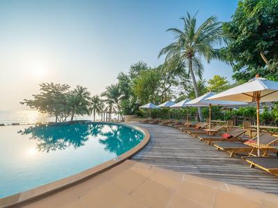 Infinity-Pool mit Sonnenliegen und Sonnenschirmen an tropischem Resort bei Sonnenuntergang.