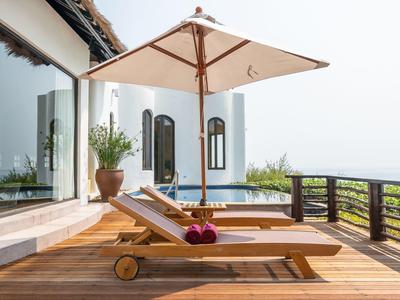 Wooden terrace with lounge chairs, parasol, and sea view under clear sky.