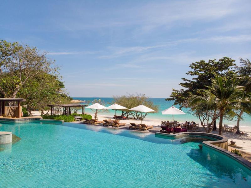 Inviting pool area with lounge chairs and umbrellas on the beach under blue sky.