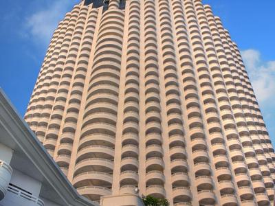 Hohes rundes Gebäude mit vielen Balkonen, blauer Himmel und weiße moderne Fassade im Vordergrund.