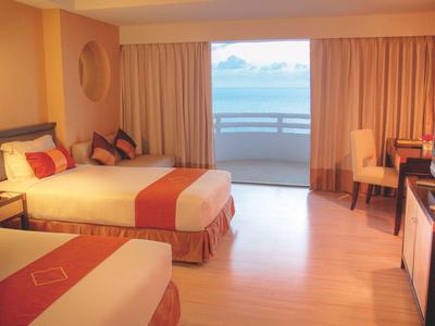 Helles Hotelzimmer mit zwei Betten, orangefarbenen Akzenten und Balkon mit Meerblick.