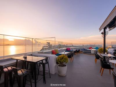 Moderne Dachterrasse mit Tischen, Stühlen und Panoramablick auf das Meer bei Sonnenuntergang.