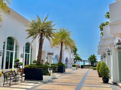 Heller Innenhof mit Palmen und Bänken zwischen weißen Gebäuden unter blauem Himmel.