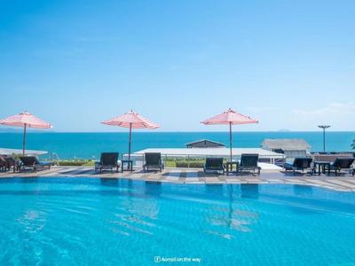 Pool mit klar blauem Wasser, pinken Sonnenschirmen und Blick auf das blaue Meer unter klarem Himmel.