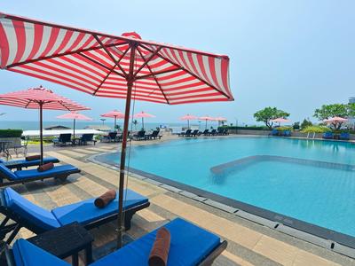 Großer Pool mit blauen Liegestühlen und rot-weißen Sonnenschirmen an sonnigem Tag.